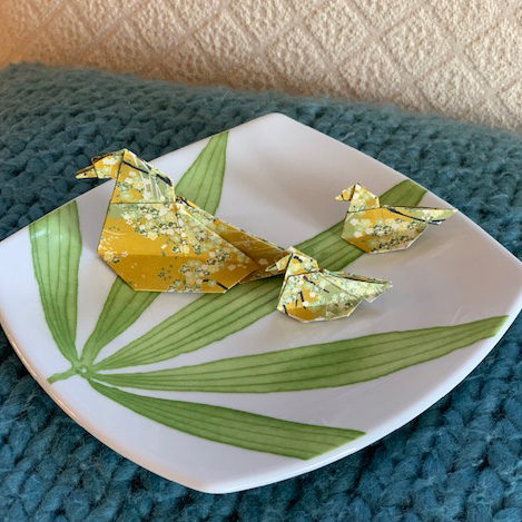 A ceramic plate with green plant motif holding three origami paper ducks